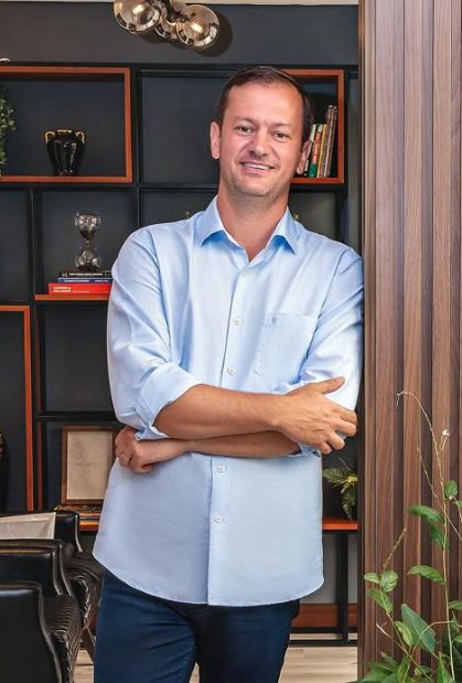 James Périco Neto em pé no escritório, de braços cruzados, sorrindo